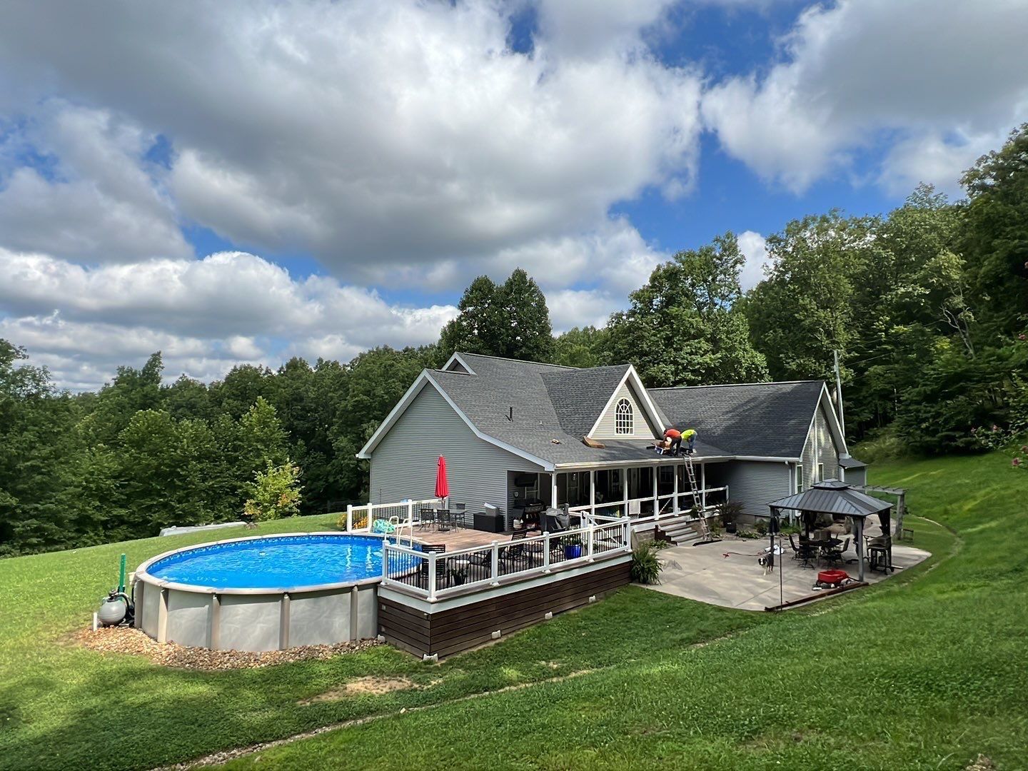 Crew installing charcoal shingles on a home with pool and deck