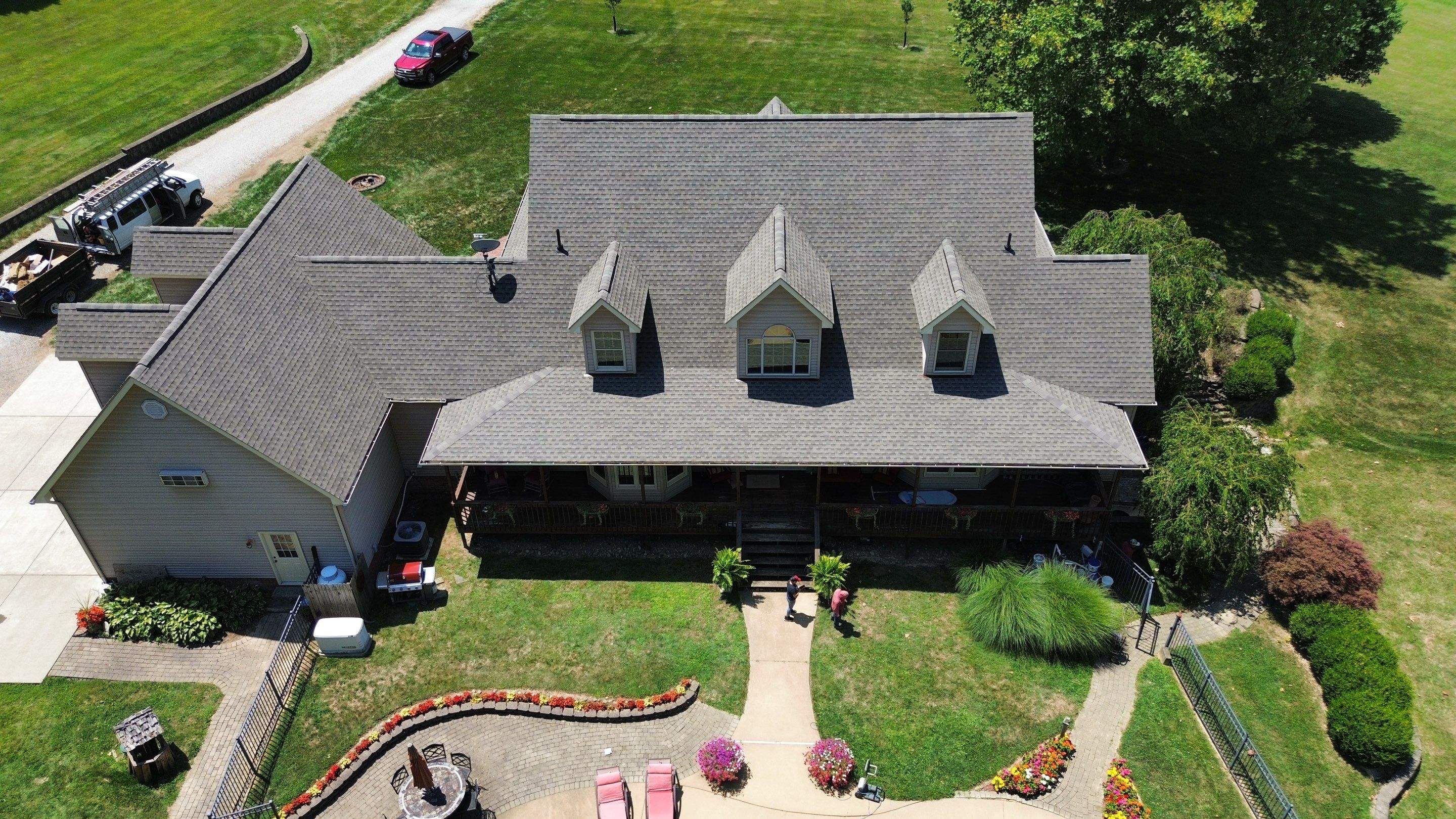 Brown shingle roof with dormers and porch on a tan home